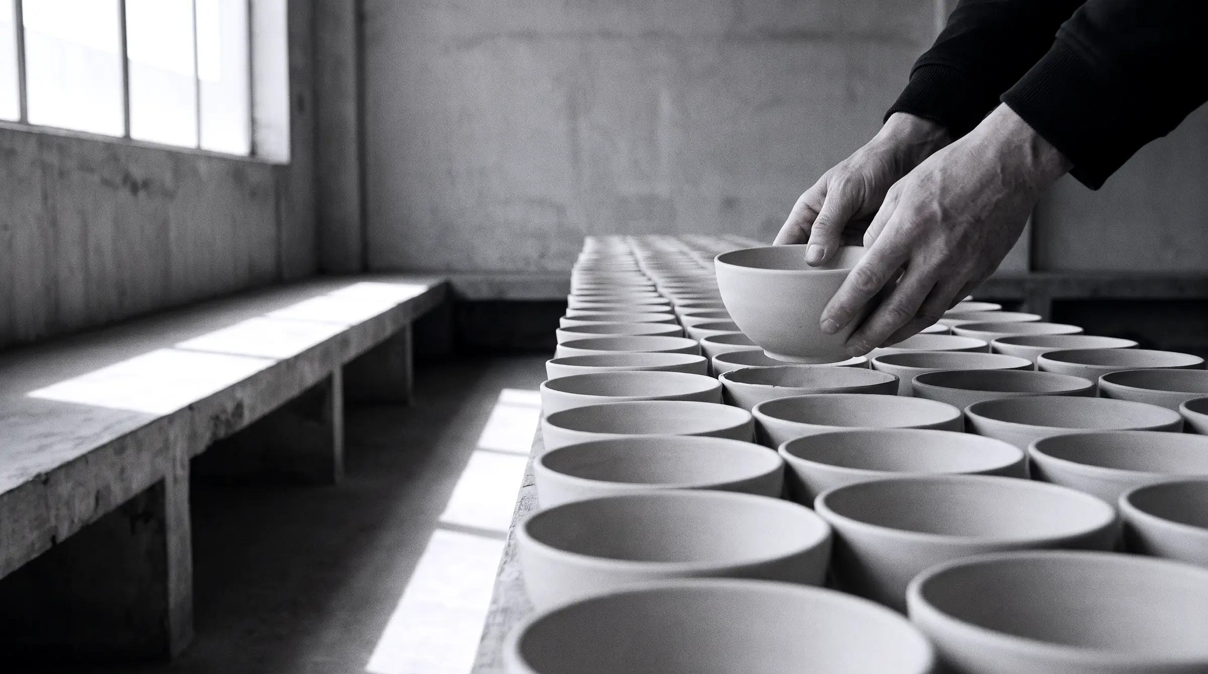 A hand lifting one bowl out of a long row of identical bowls